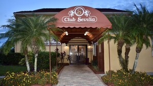 The Club Sevilla building with a covered entrance, palm trees, and flower beds. - Club Sevilla (Kissimmee)