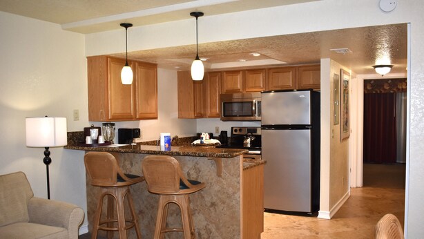 A kitchen with wooden cabinets, a microwave, a refrigerator, and two bar stools. - Club Sevilla (Kissimmee)