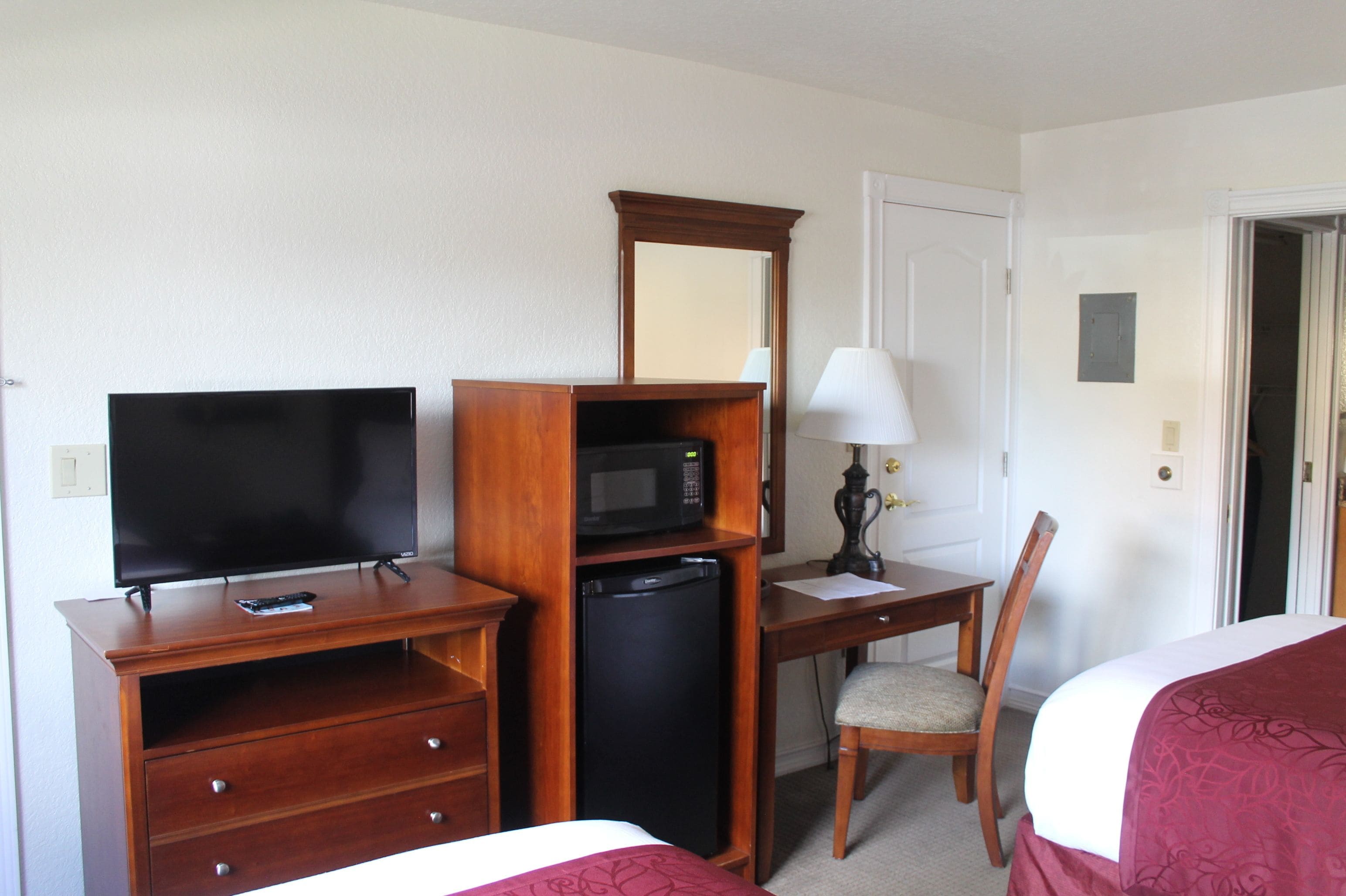 A hotel room with a bed, a desk with a lamp, a television, a microwave, and a refrigerator.