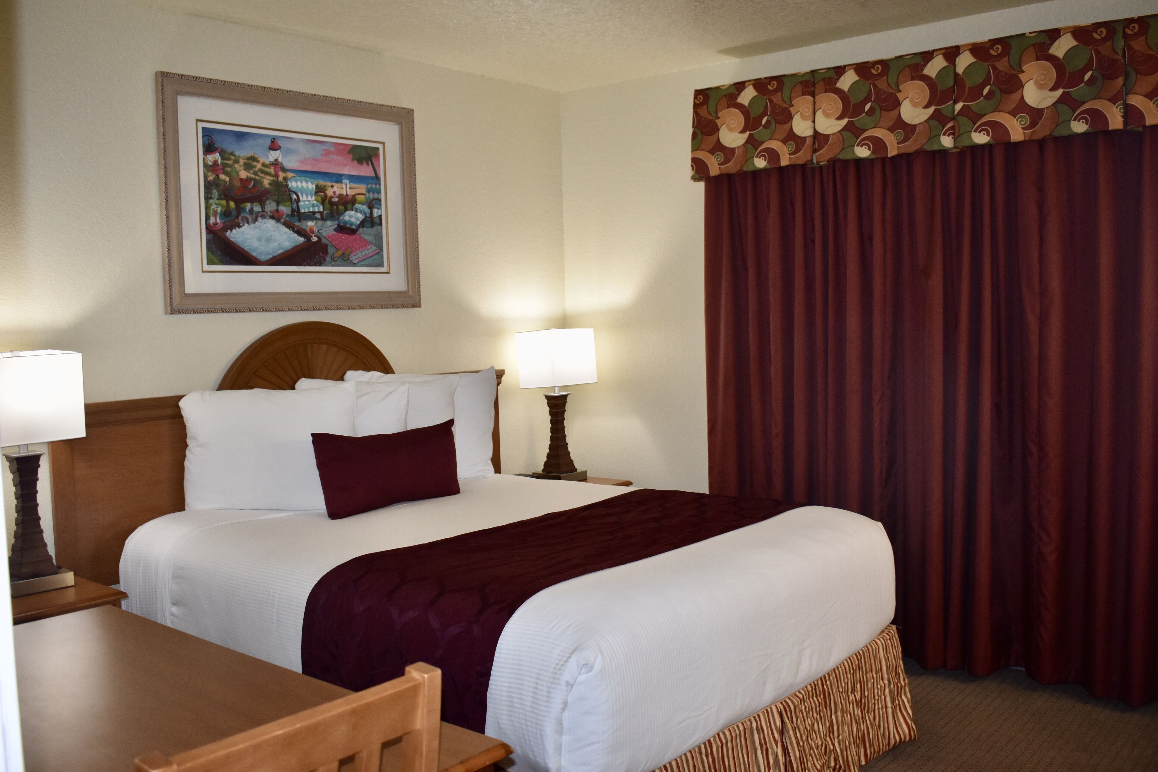 A hotel room with a large bed, two bedside tables, a desk, and a framed picture on the wall.