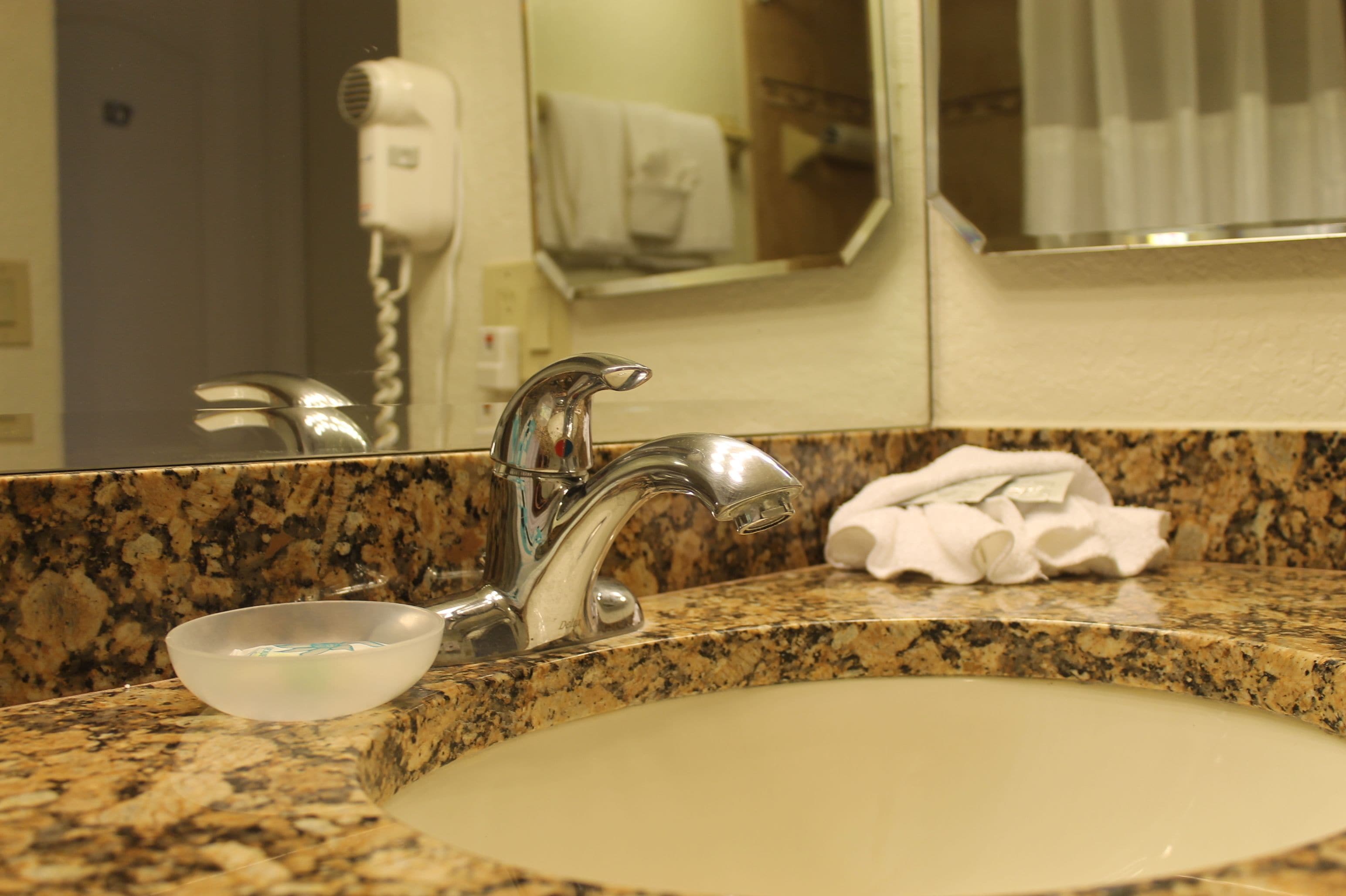 Un lavabo de salle de bain avec un plan de toilette en granit, un miroir et un sèche-cheveux fixé au mur.