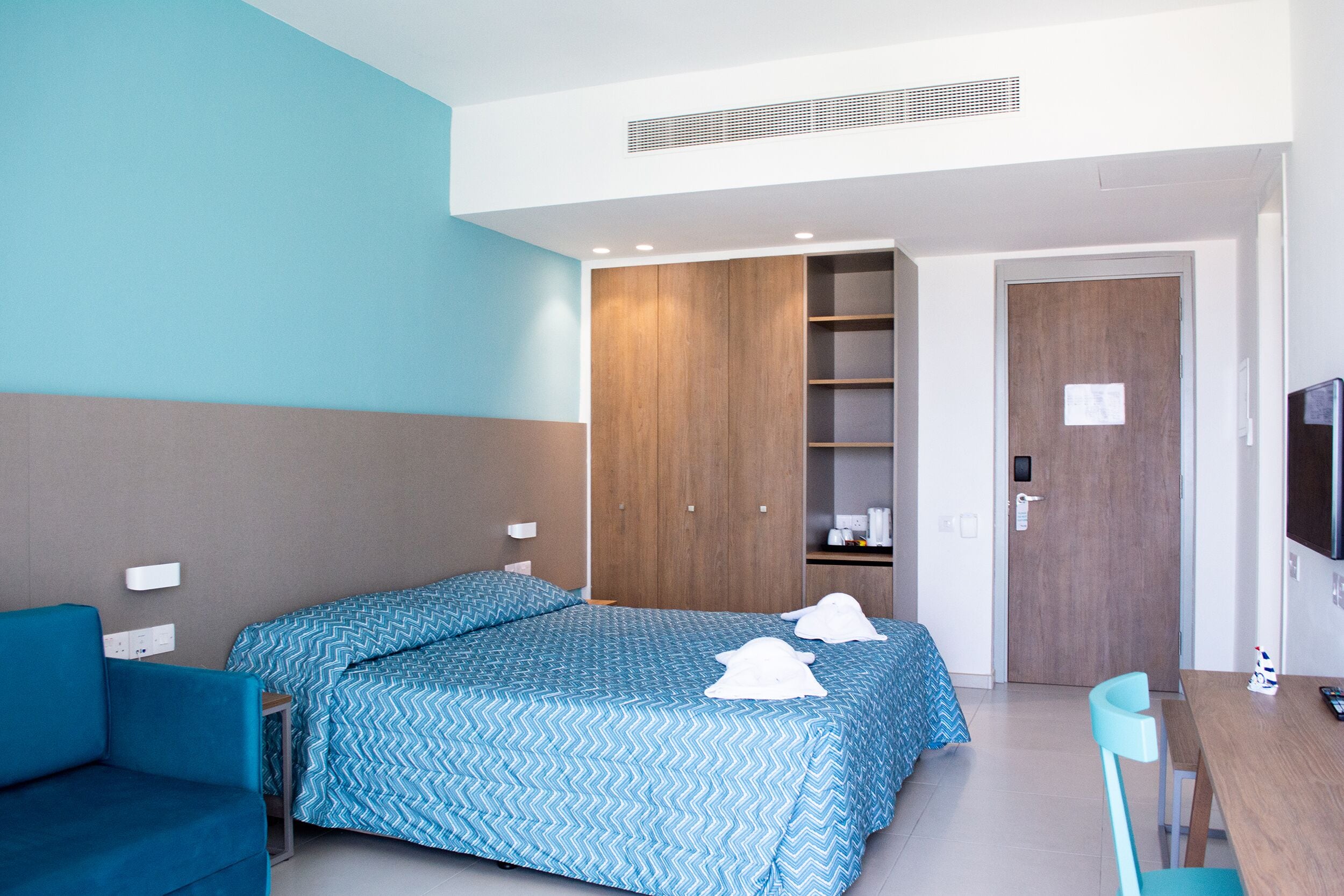 A hotel room with two beds, a desk, a chair, a TV, and a wardrobe.