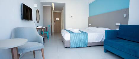 A hotel room with a bed, a blue sofa, a small table, a chair, and a TV mounted on the wall.