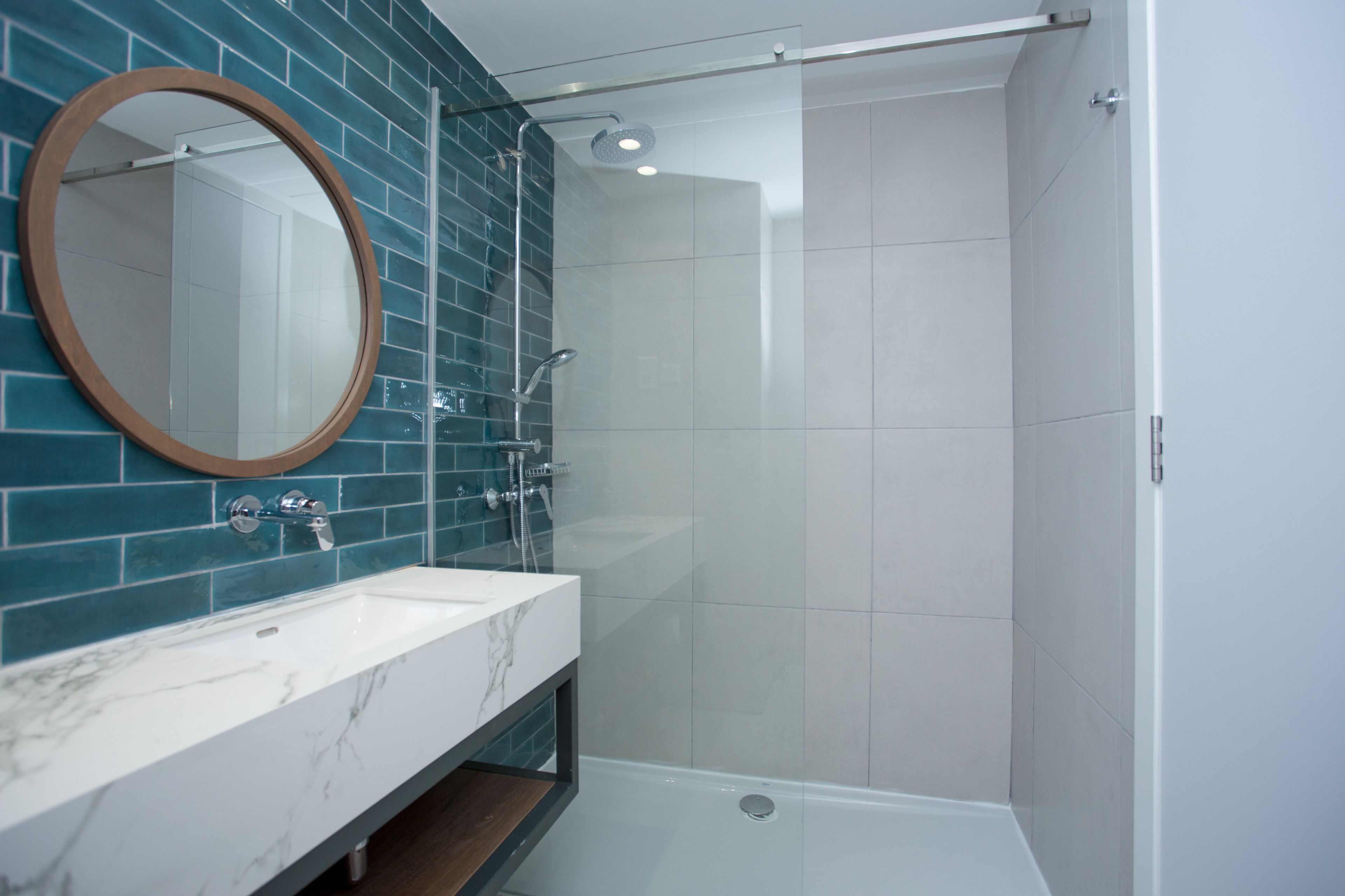 Un baño moderno con ducha envuelta en vidrio, lavabo de mármol y paredes con azulejos color aguamarina.