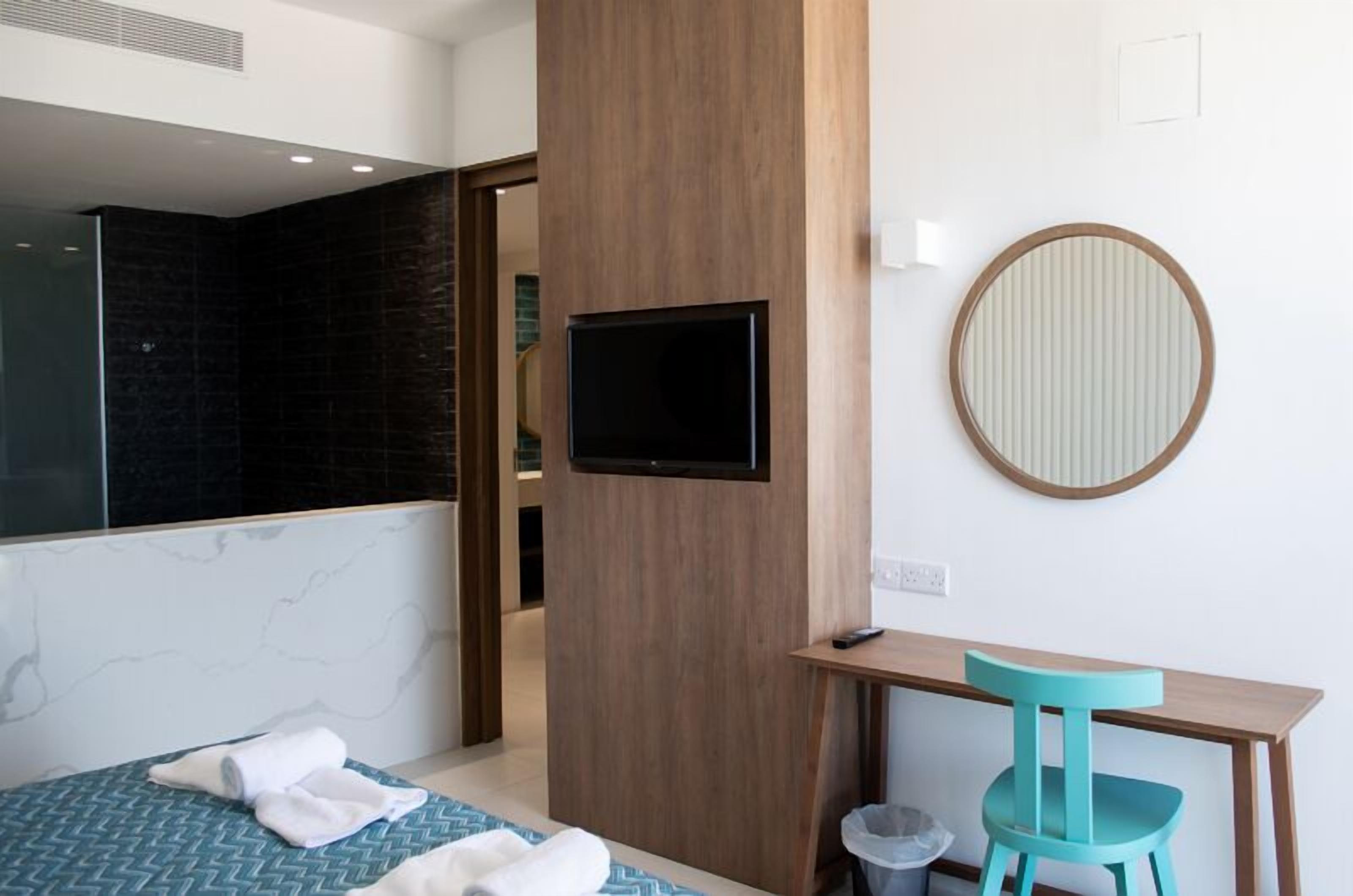 A hotel room with a bed, a desk, a chair, a television, and a mirror.