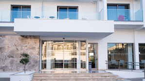 Un bâtiment moderne avec une entrée en verre, un petit arbre et un escalier menant à l’entrée.