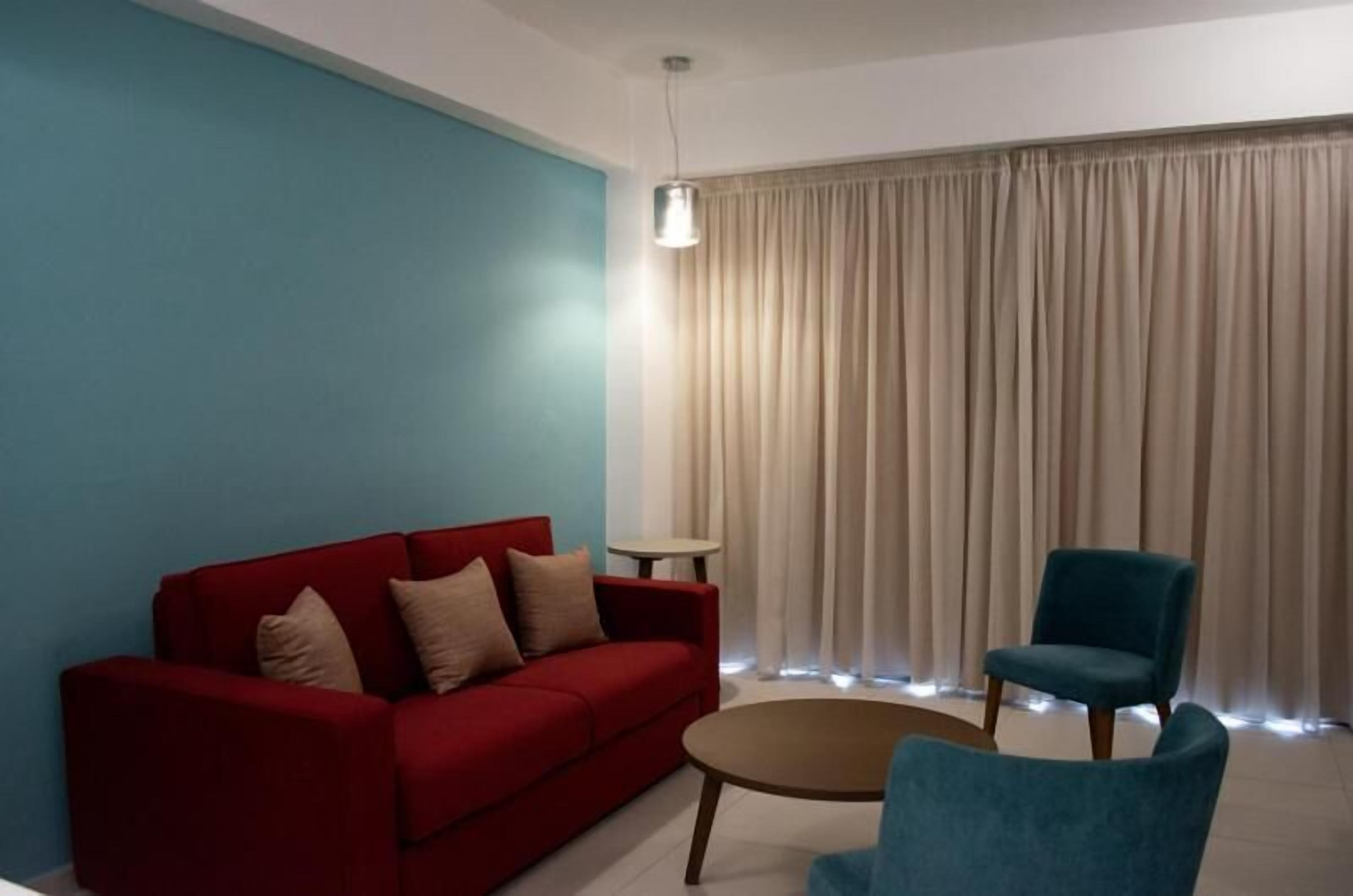 Una sala de estar con un sofá rojo, un sillón azul, una mesita redonda y una lámpara de pie.