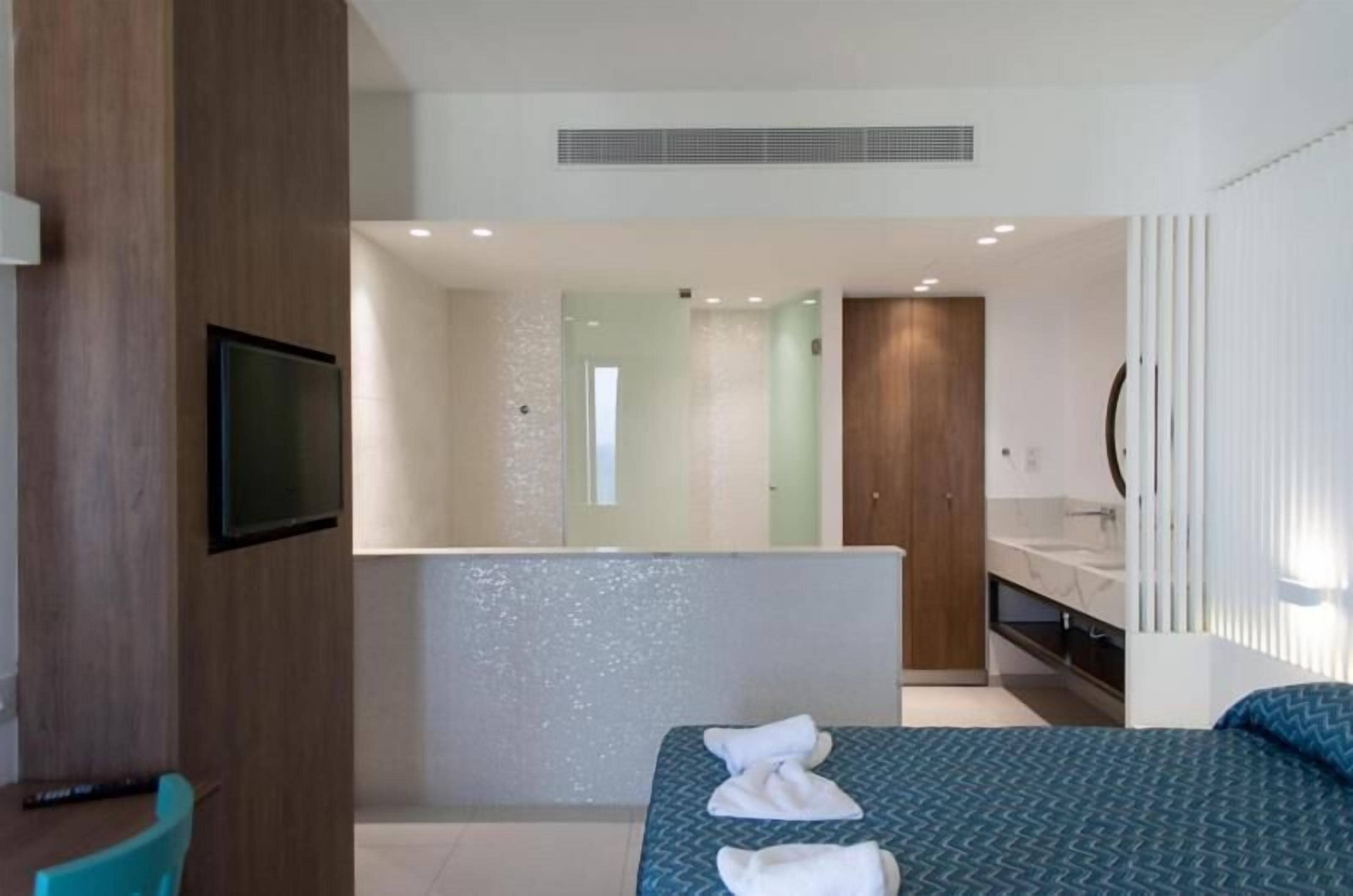 Une chambre d’hôtel moderne, équipée d’un lit, d’une télévision, d’une salle de bain avec un miroir et d’un panneau en bois sur le mur.