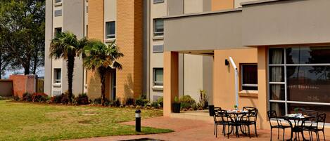 A modern hotel with a swimming pool, outdoor seating, and a well-maintained garden.