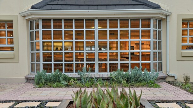 Un edificio con un amplio ventanal y un jardín con plantas al frente.