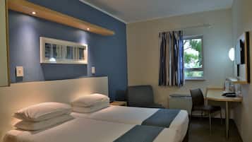 Une chambre d’hôtel avec deux lits, un bureau, une chaise, une fenêtre avec des rideaux et un téléviseur fixé au mur.