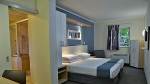 Una habitación de hotel moderna con cama, escritorio, silla, armario y zona de ducha.