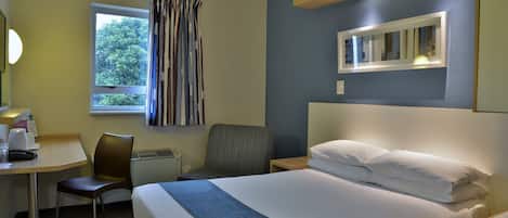 Une chambre d’hôtel avec un lit, un bureau, une chaise, une fenêtre avec des rideaux et un miroir au mur.