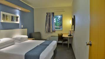 Habitación de hotel con cama, escritorio, silla y ventana con cortinas.