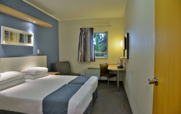 Habitación de hotel con cama, escritorio, silla y ventana con cortinas.