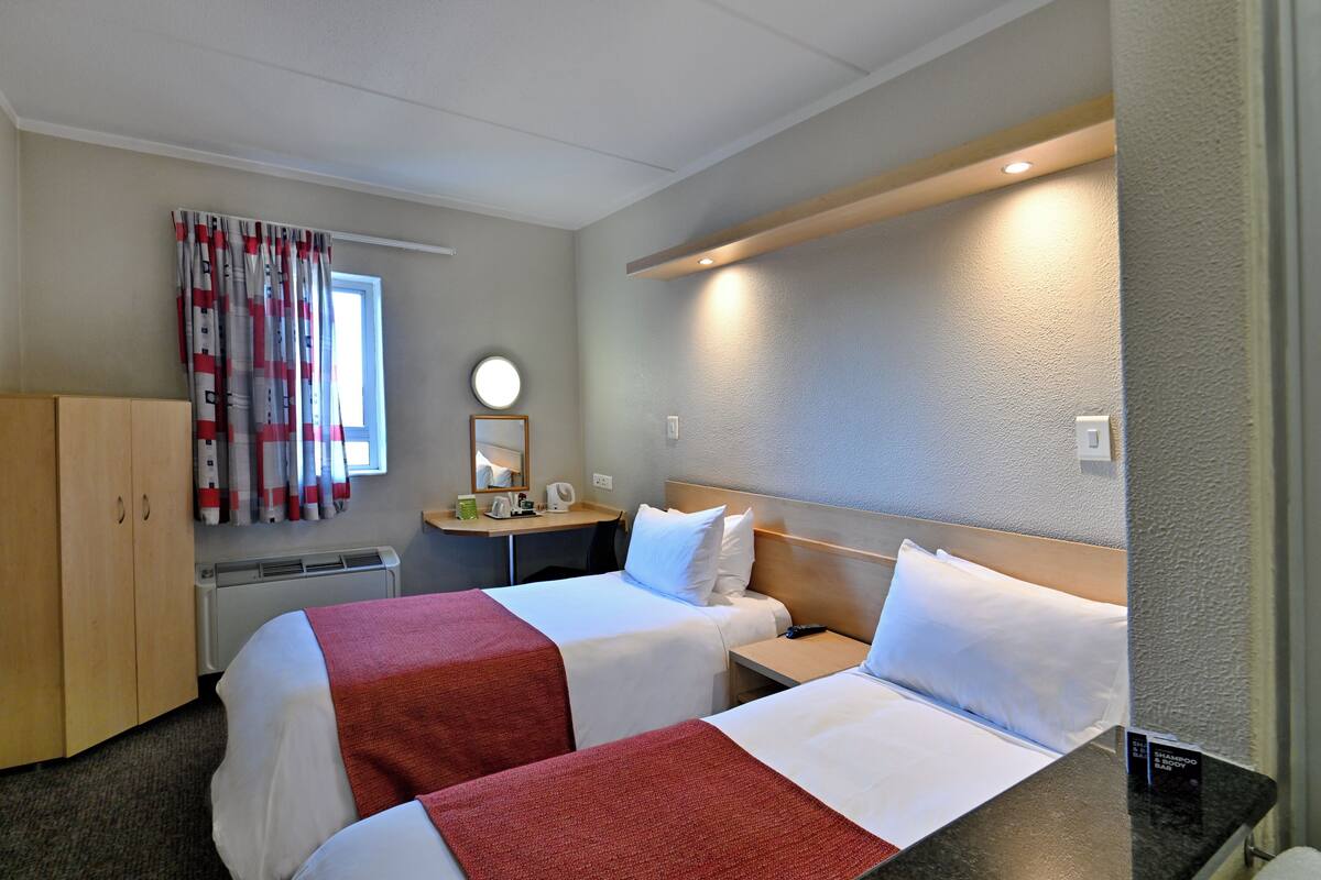 A hotel room with two beds, a desk, a mirror, and a window with curtains.