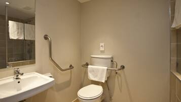 Une salle de bain avec un lavabo blanc, des toilettes et des barres d’appui.