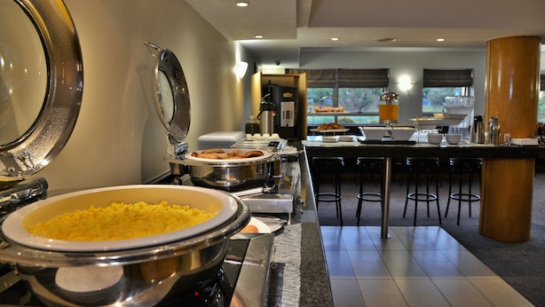 A buffet setup with various food items and a coffee station in a modern hotel dining area.