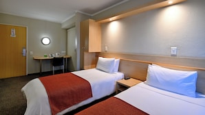 A hotel room with two beds, a desk, and a chair.