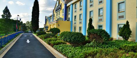 A hotel with a road leading to it, surrounded by greenery and a blue fence.