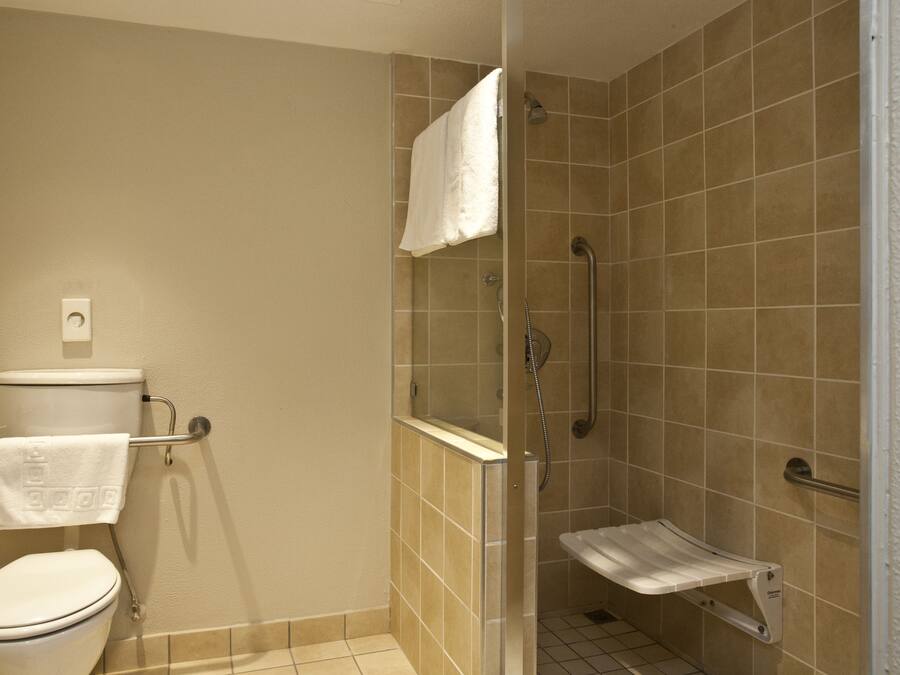 Baño con inodoro, cabina de ducha y barra de apoyo.
