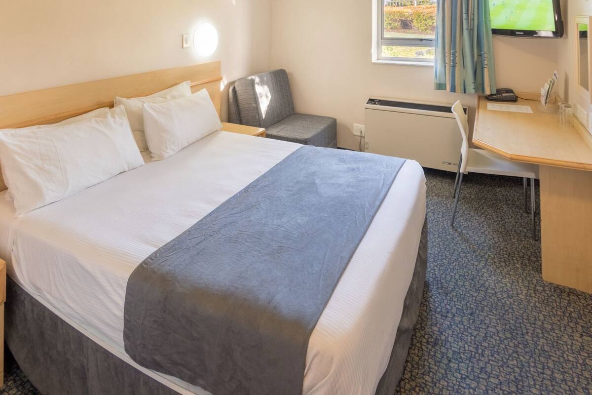 Une chambre d’hôtel équipée d’un lit, d’un bureau, d’une chaise, d’une télévision et d’une fenêtre avec des rideaux.