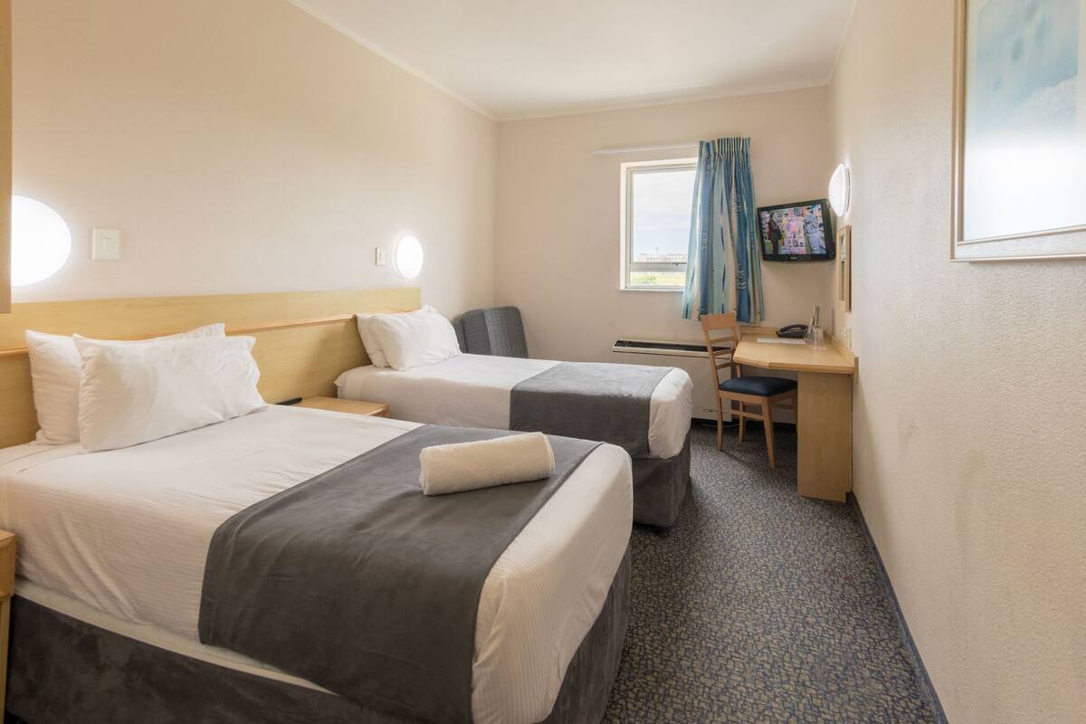Une chambre d’hôtel avec deux lits, un bureau, une chaise, une télévision et une fenêtre avec des rideaux.