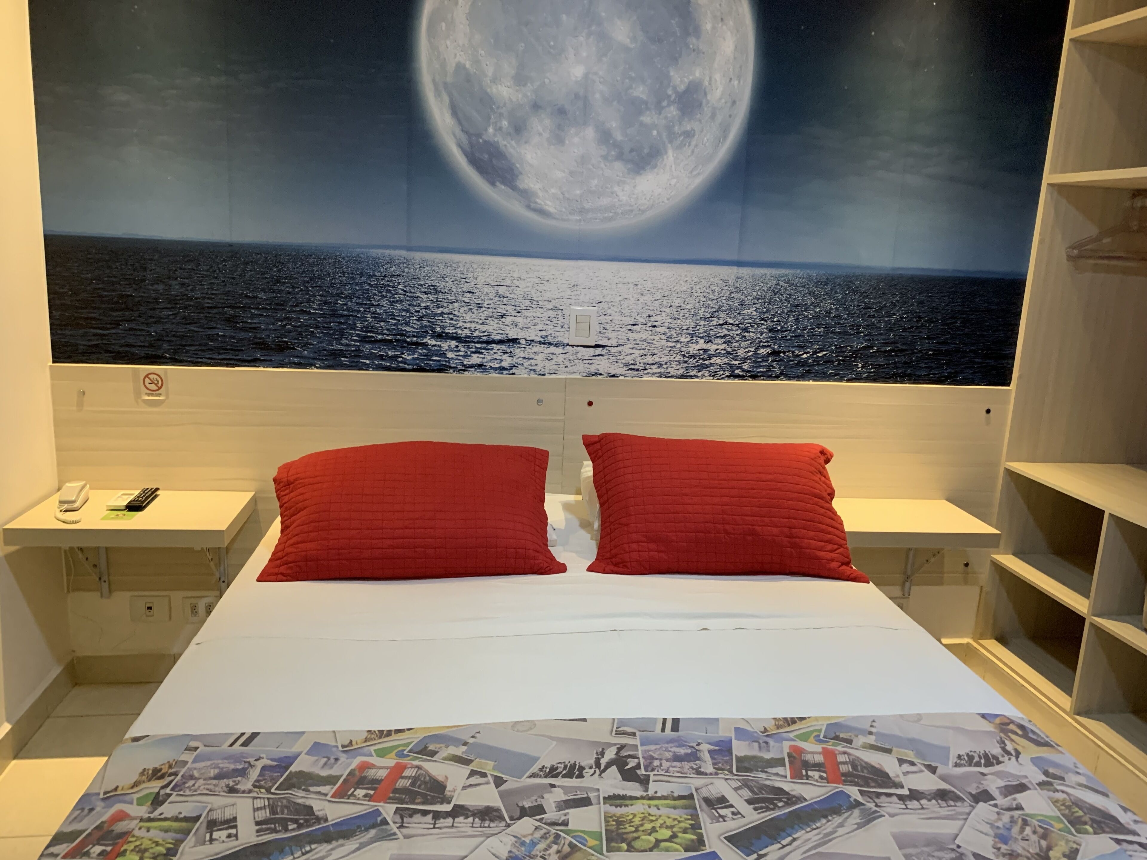 A hotel room with a large bed, two red pillows, a nightstand with a phone, and a wall mural of a moonlit sea.