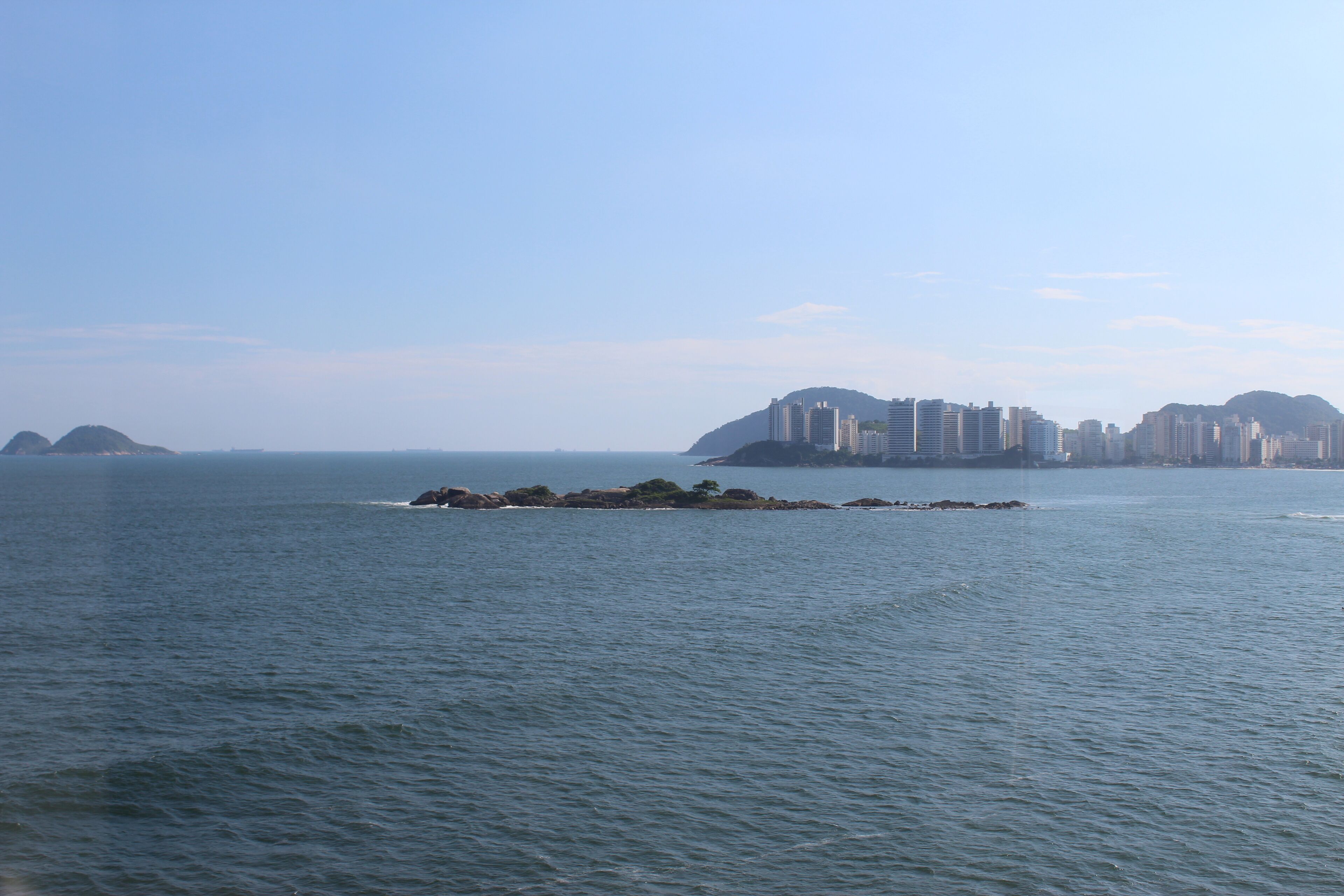 A coastal cityscape with a prominent cluster of high-rise buildings on a peninsula, surrounded by calm sea waters.