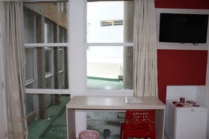 Quarto com janela, escrivaninha, cadeira vermelha e pequena geladeira.