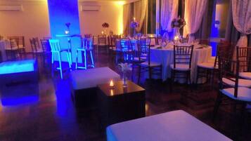 Un comedor de hotel con mesas dispuestas para el servicio, sillas alrededor y una zona de bar con taburetes.
