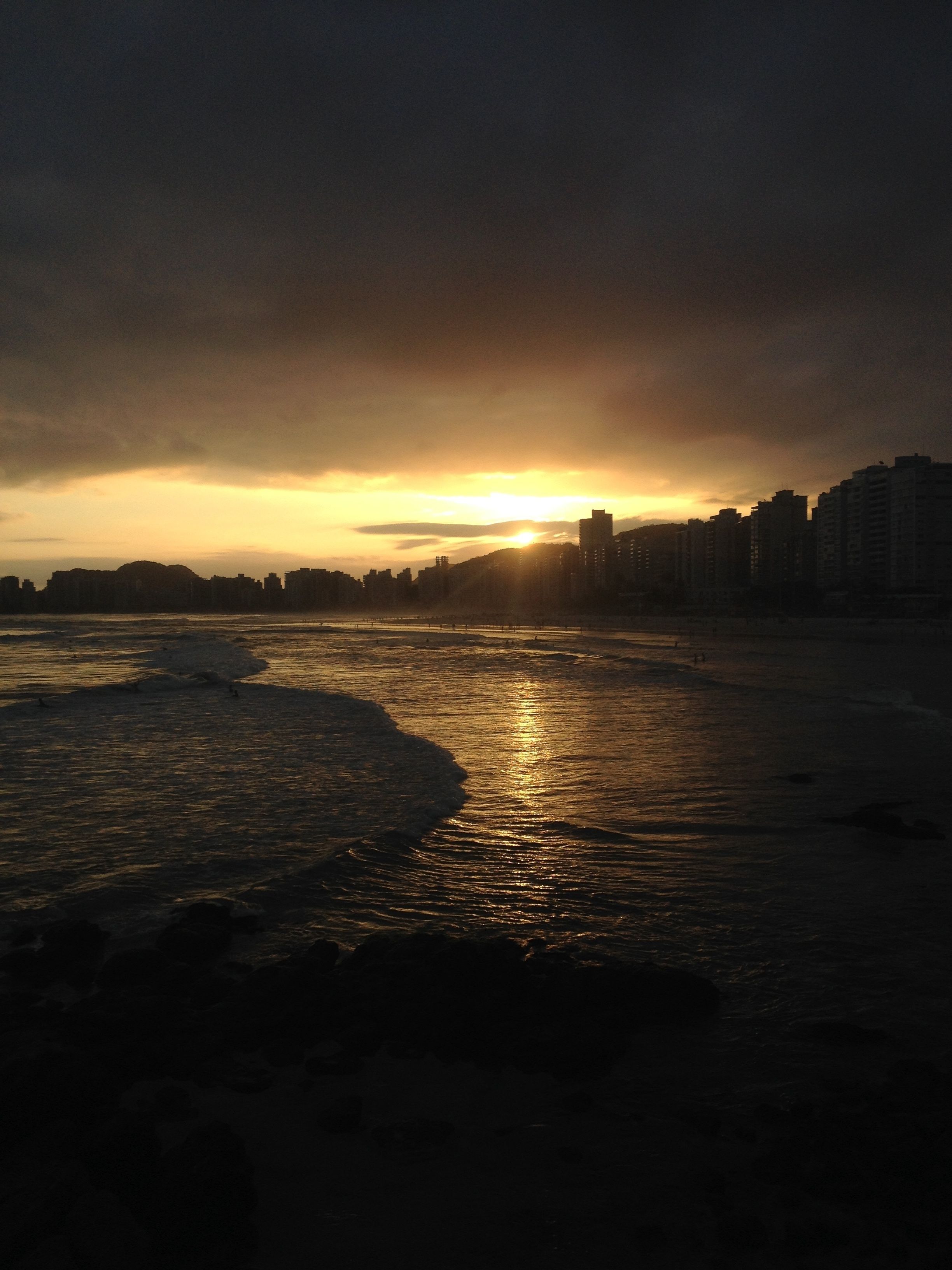 A beach with a sunset in the background and buildings along the shore.