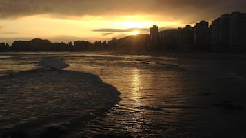 A beach with a sunset in the background and buildings along the shore.