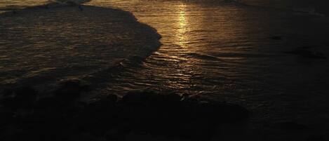 A beach with a sunset in the background and buildings along the shore.