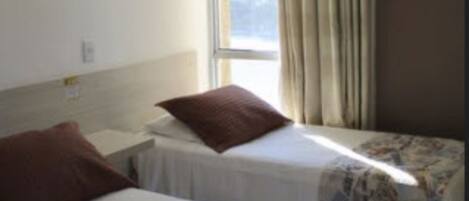 Ein Hotelzimmer mit zwei Einzelbetten, einem fenster mit Vorhängen und Blick auf die Stadtlandschaft.