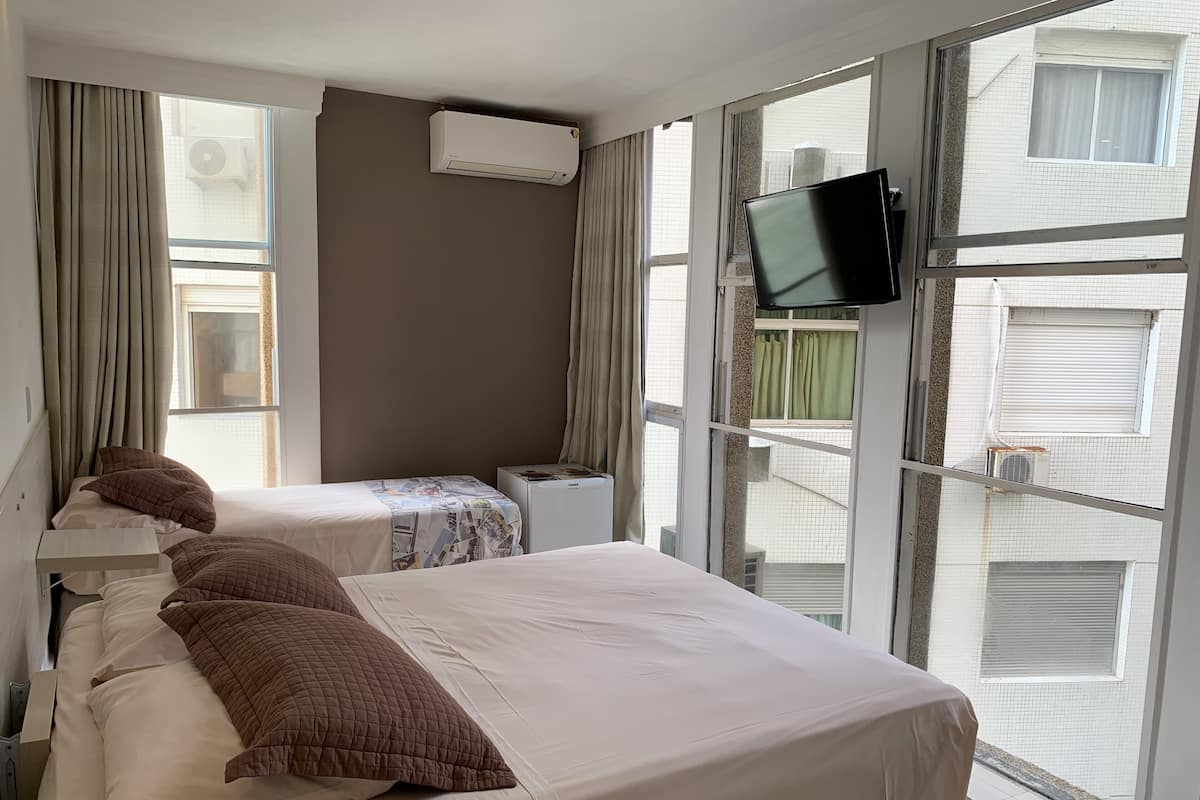 A hotel room with two beds, a TV mounted on the wall, and large windows with curtains.