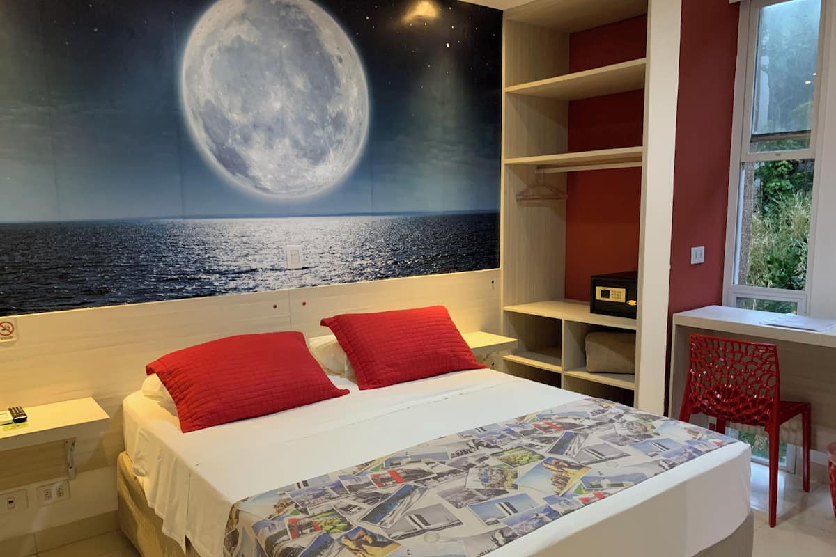 A bedroom with a large bed, red pillows, a night sky mural, a desk, and a chair.