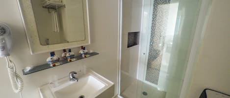 A bathroom with a glass shower enclosure, a sink, a mirror, and a hairdryer.