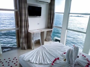 A room with a bed, a TV mounted on the wall, and a view of the sea. - Grand Hotel Guaruja (Guarujá)