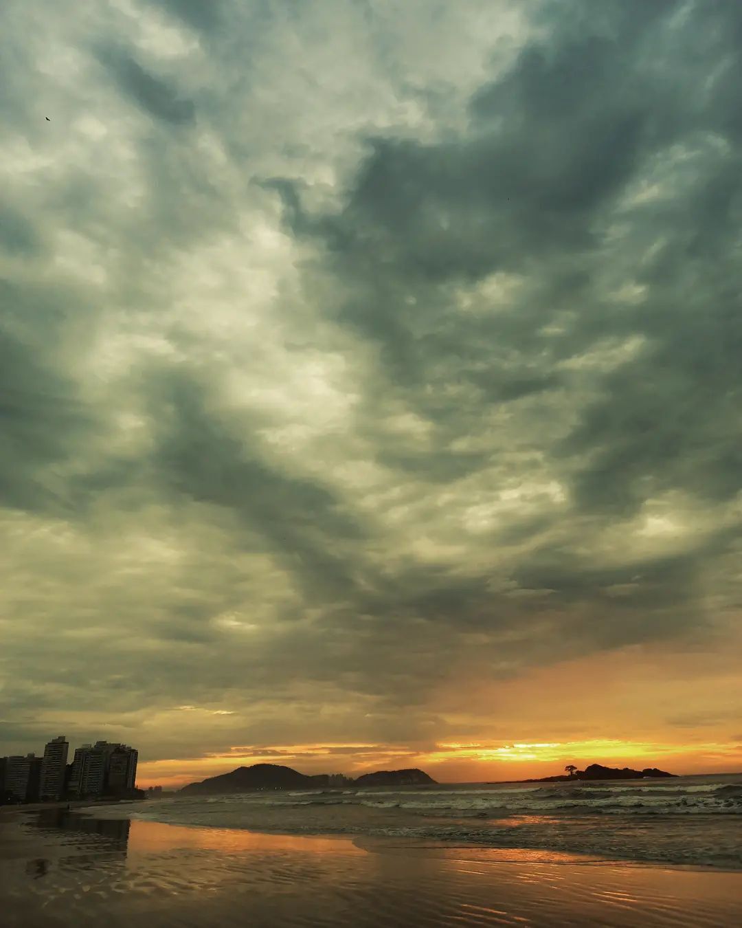 Una playa con cielo nublado y un atardecer.