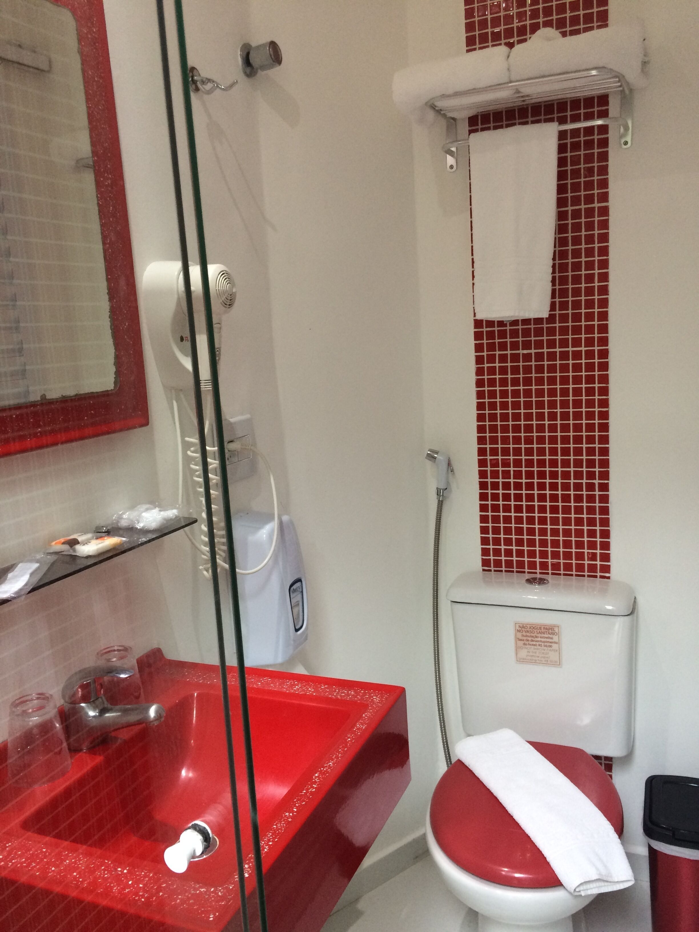 A bathroom with a red sink, a glass shower enclosure, a white toilet, and a red-tiled shower wall.