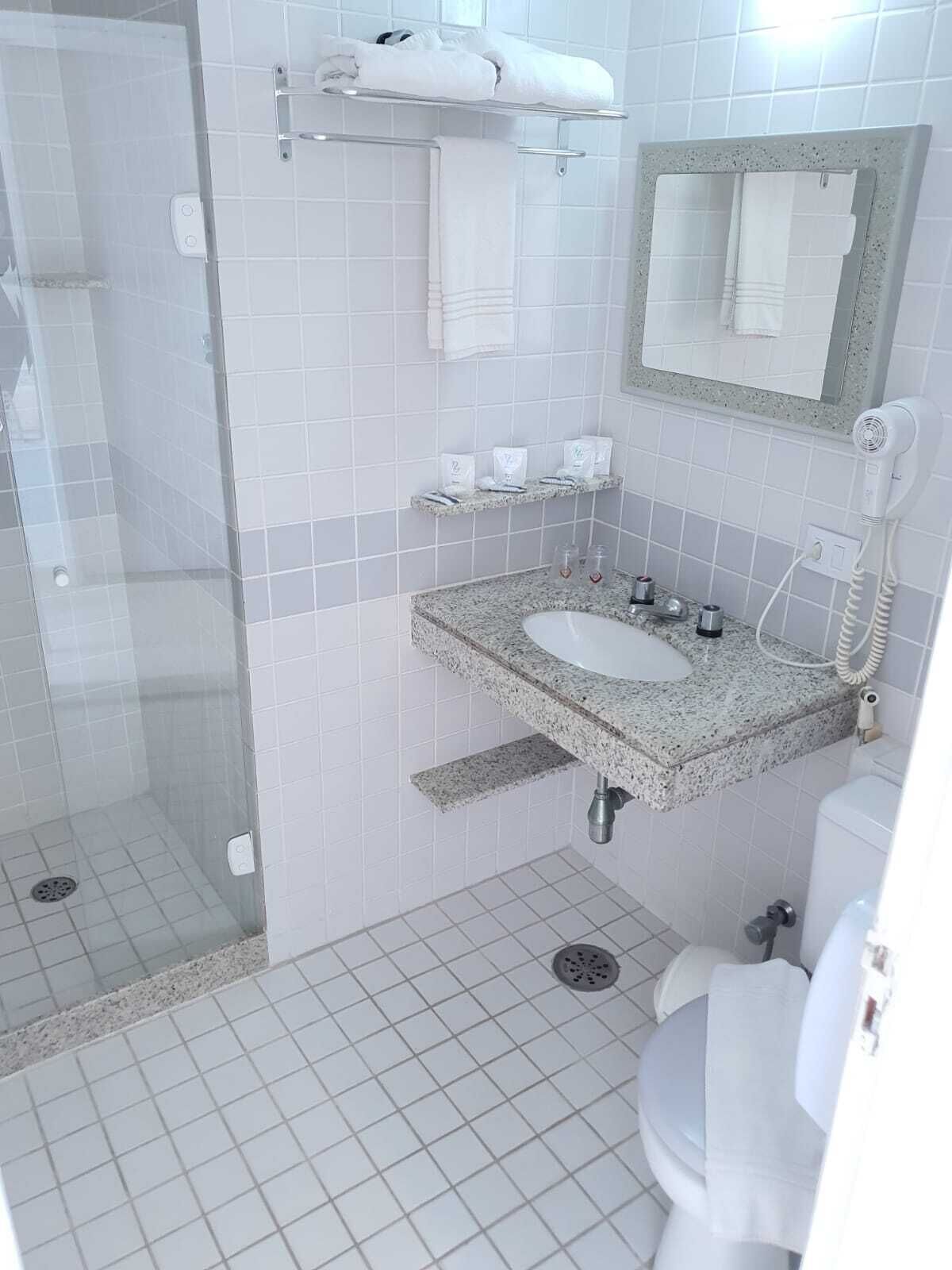 Une salle de bain avec une douche à parois de verre, un lavabo sur un plan de travail en granit, des toilettes et un sèche-cheveux fixé au mur.