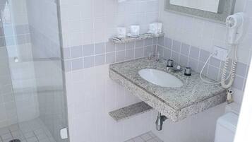Une salle de bain avec une douche à parois de verre, un lavabo sur un plan de travail en granit, des toilettes et un sèche-cheveux fixé au mur.