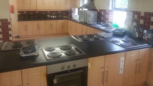 A kitchen with wooden cabinets, a black countertop, a stove, and a window. - Courtbrack Accommodation - Hostel (Limerick)