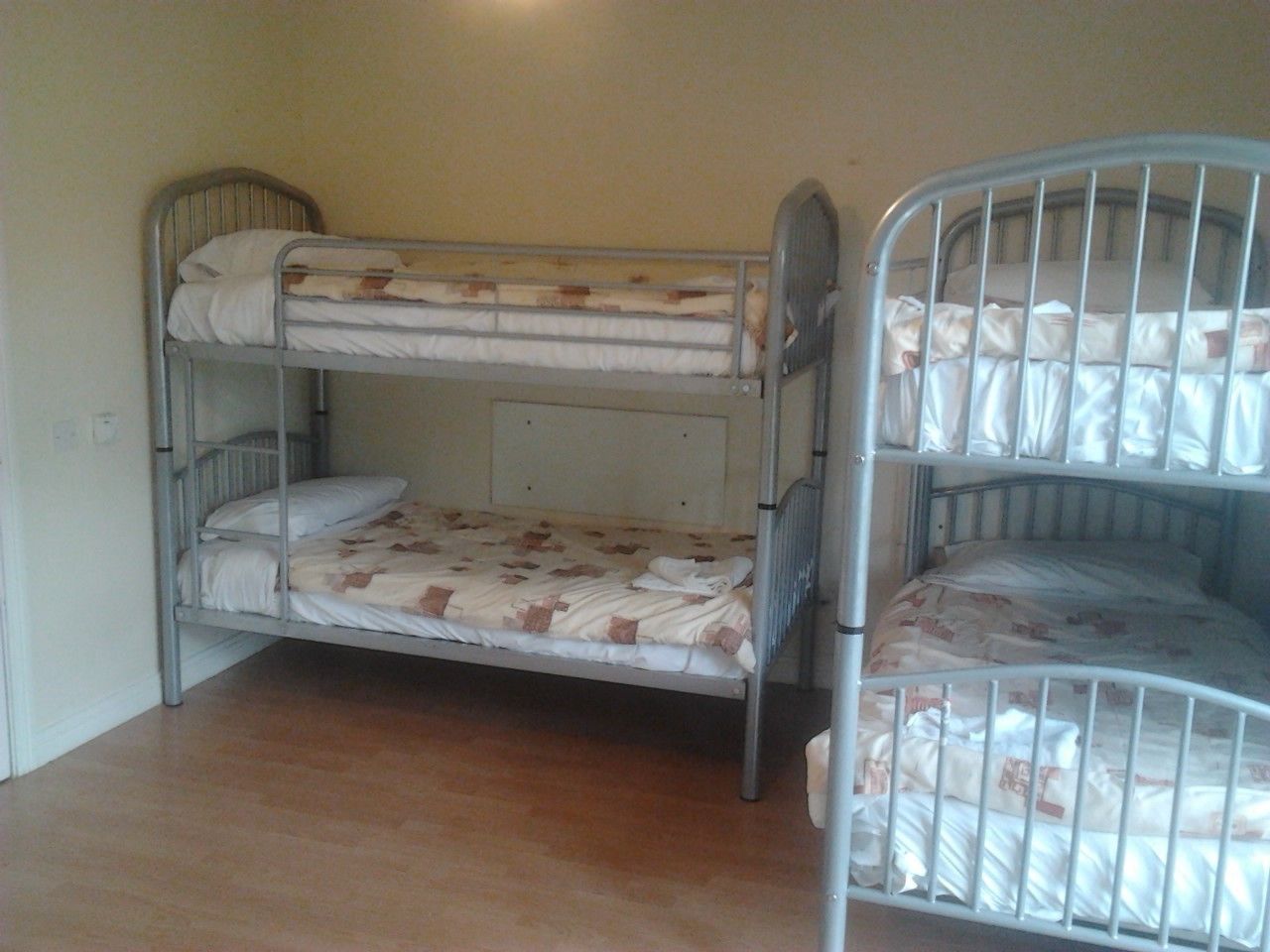 A bunk bed room with two beds, wooden flooring, and a plain wall.