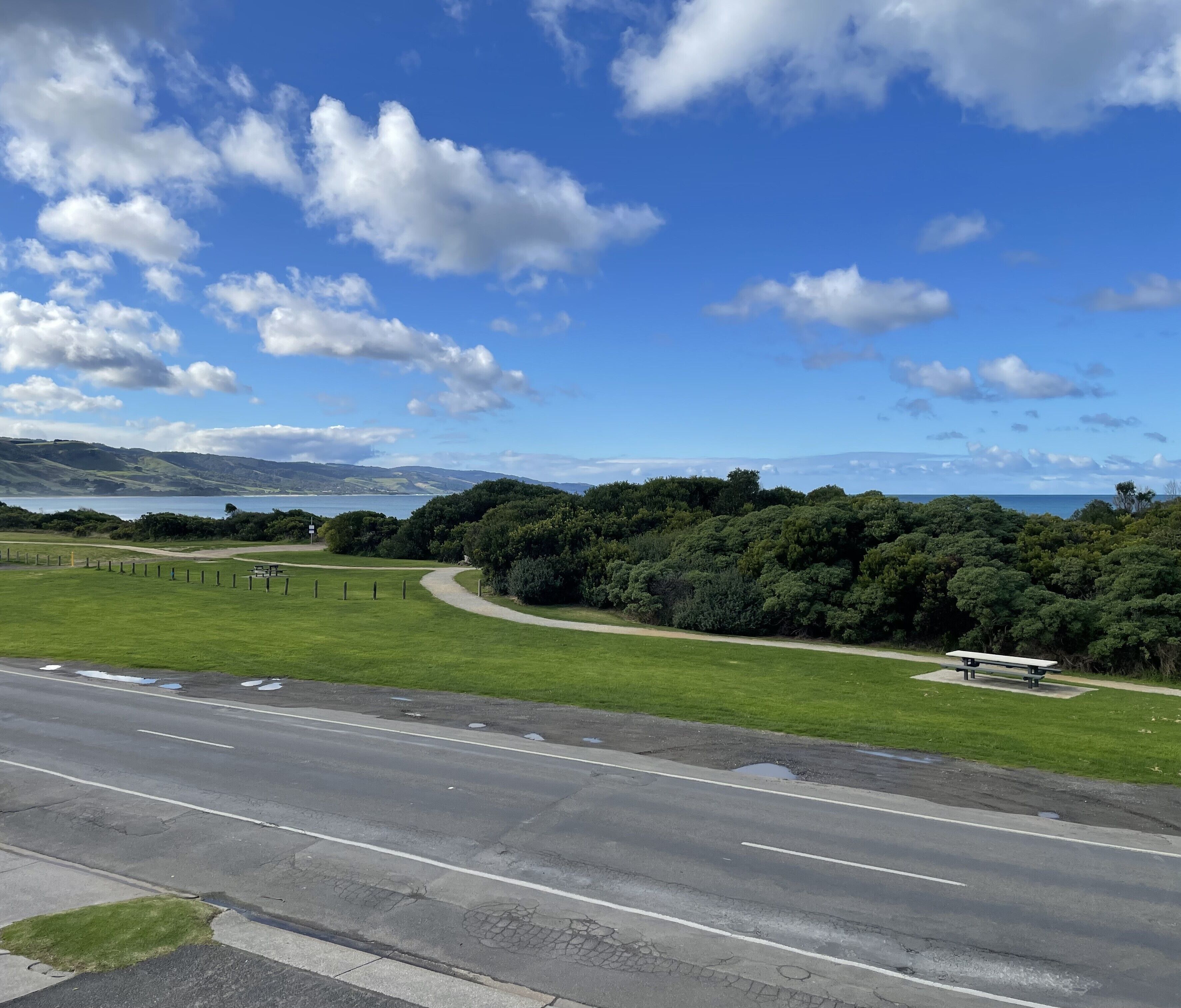 A coastal road with a grassy area and a bench.