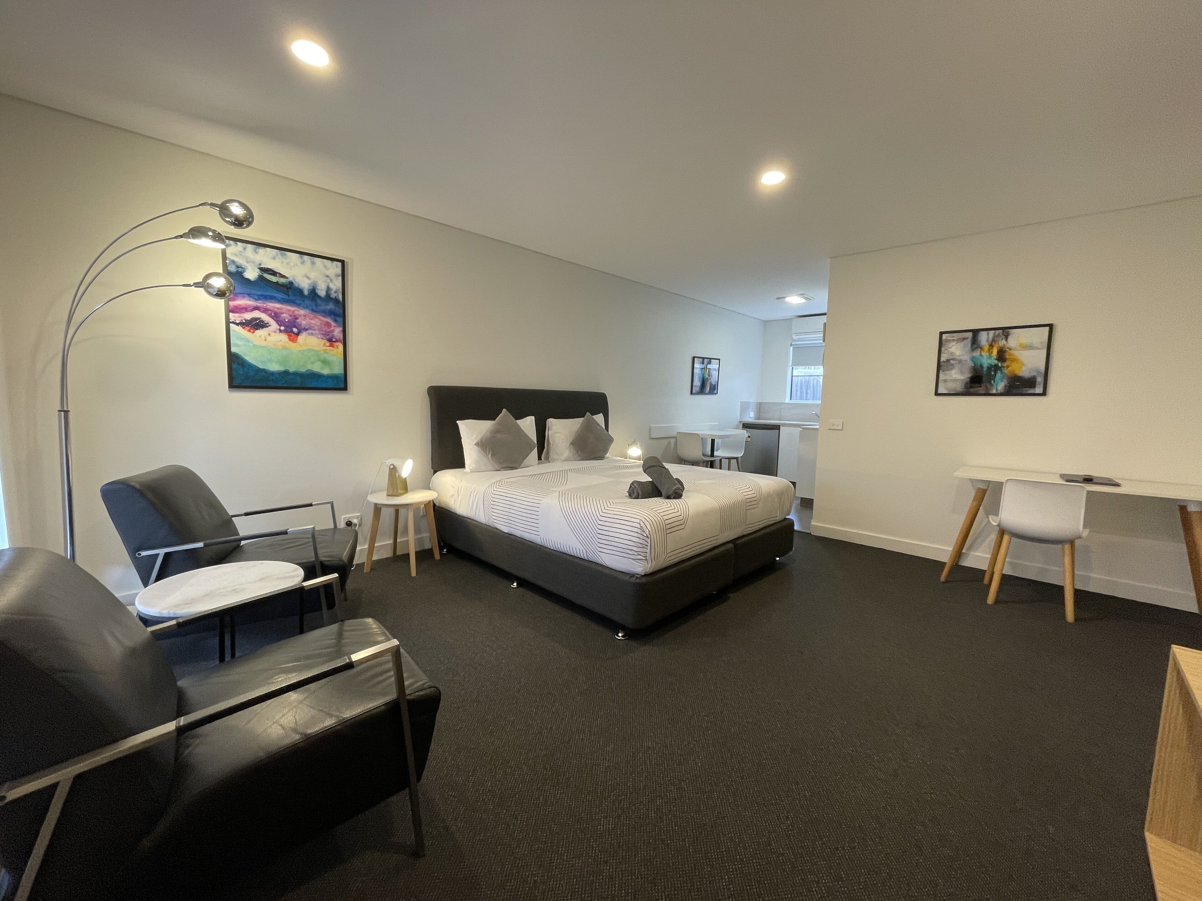Una habitación de hotel moderna con una cama grande, un escritorio, una silla y una lámpara de escritorio.