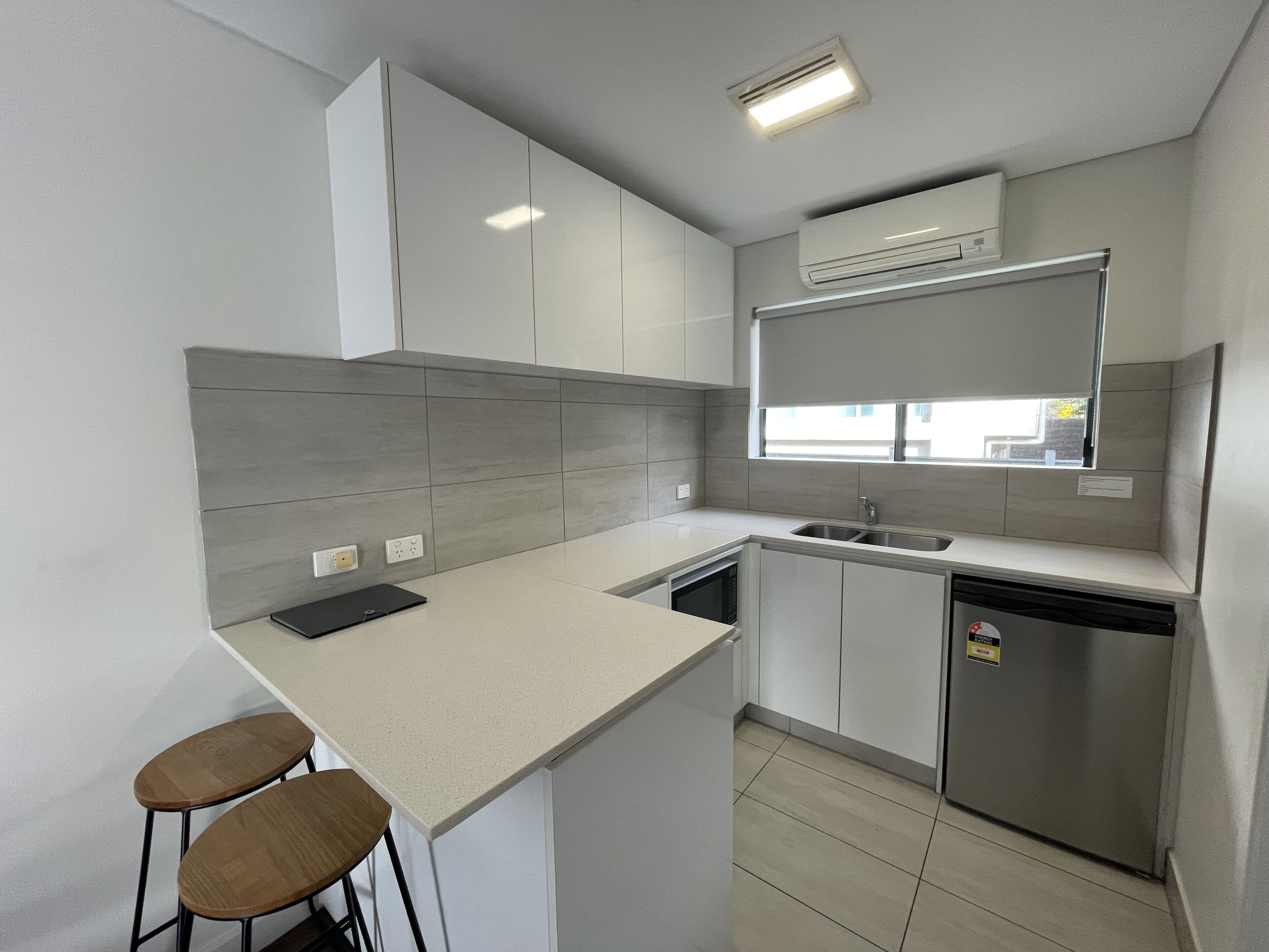 Una cocina moderna con barra, dos taburetes, lavavajillas y aire acondicionado.