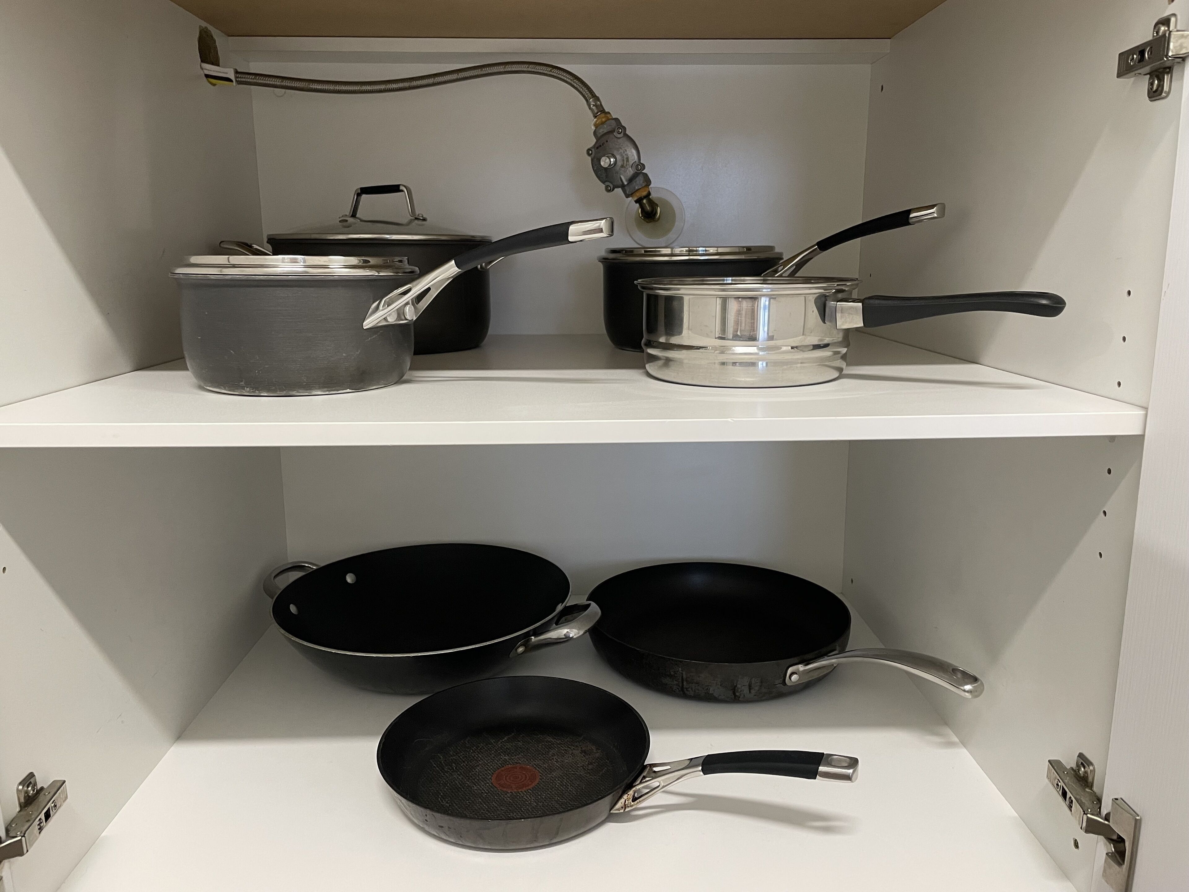 A kitchen with a white shelf holding pots and pans.