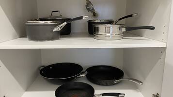 A kitchen with a white shelf holding pots and pans.